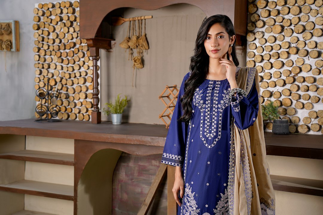 Woman in a blue embroidered dress with a tan shawl