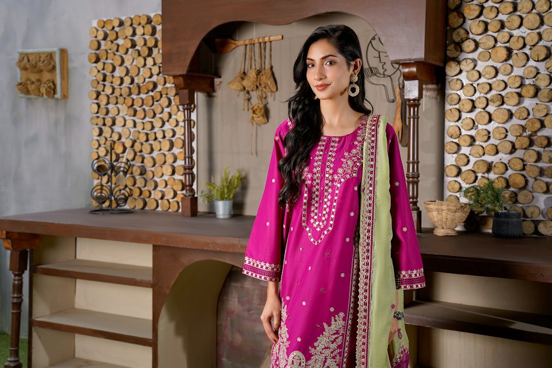 Woman in a vibrant pink embroidered dress stands indoors